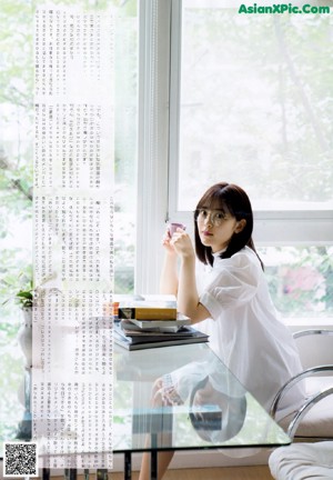 A woman standing in front of a white brick wall holding a book.