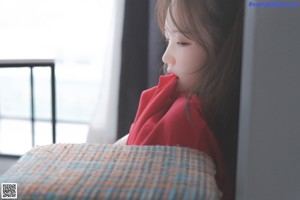 A woman in a red hoodie sitting on a stool.