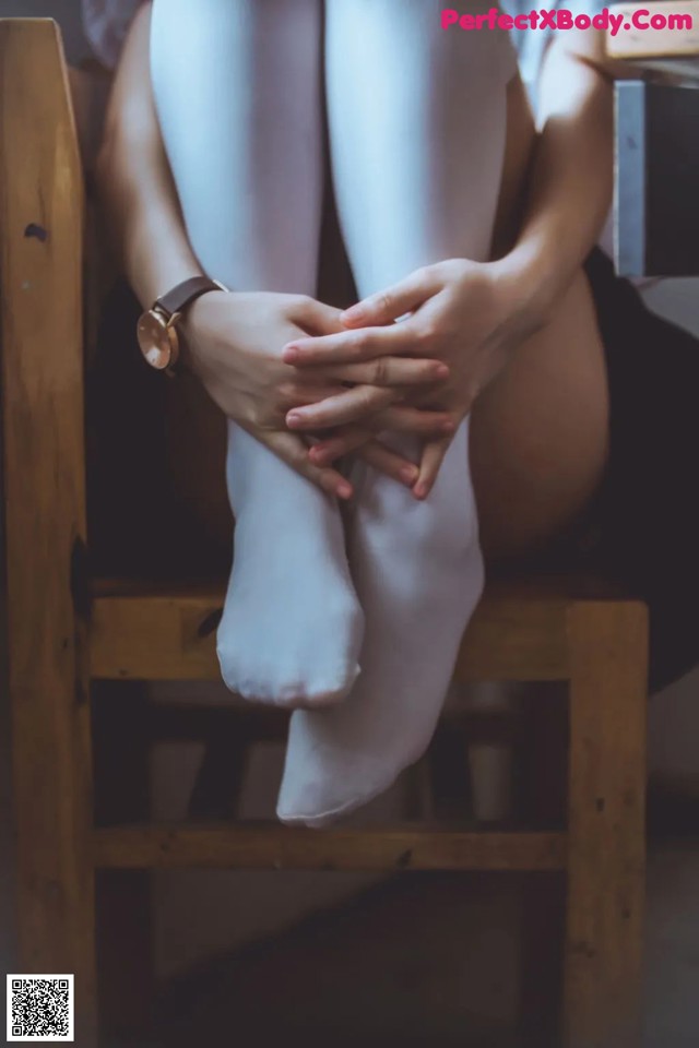 A woman sitting on a wooden chair with her legs crossed.