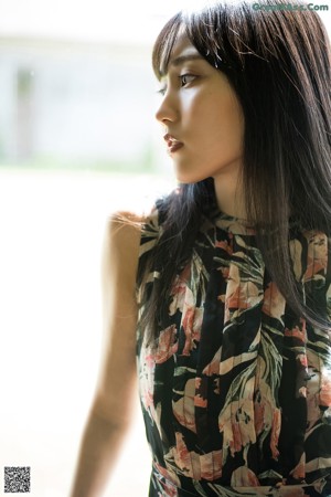 A woman in a floral dress standing in front of a window.