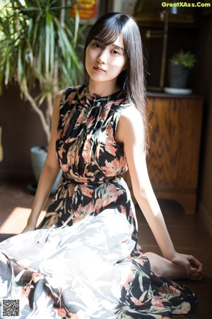 A woman in a floral dress leaning against a window.