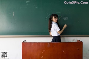 A woman sitting on top of a desk in a classroom.