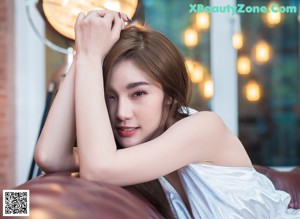 A woman in a white dress sitting on a brown couch.
