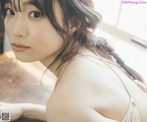 A woman in a pink tank top leaning against a wall.