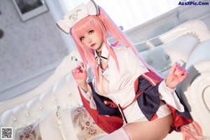 A woman with long pink hair sitting on a white couch.